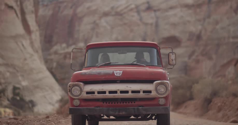A red truck is driving down a road in a canyon