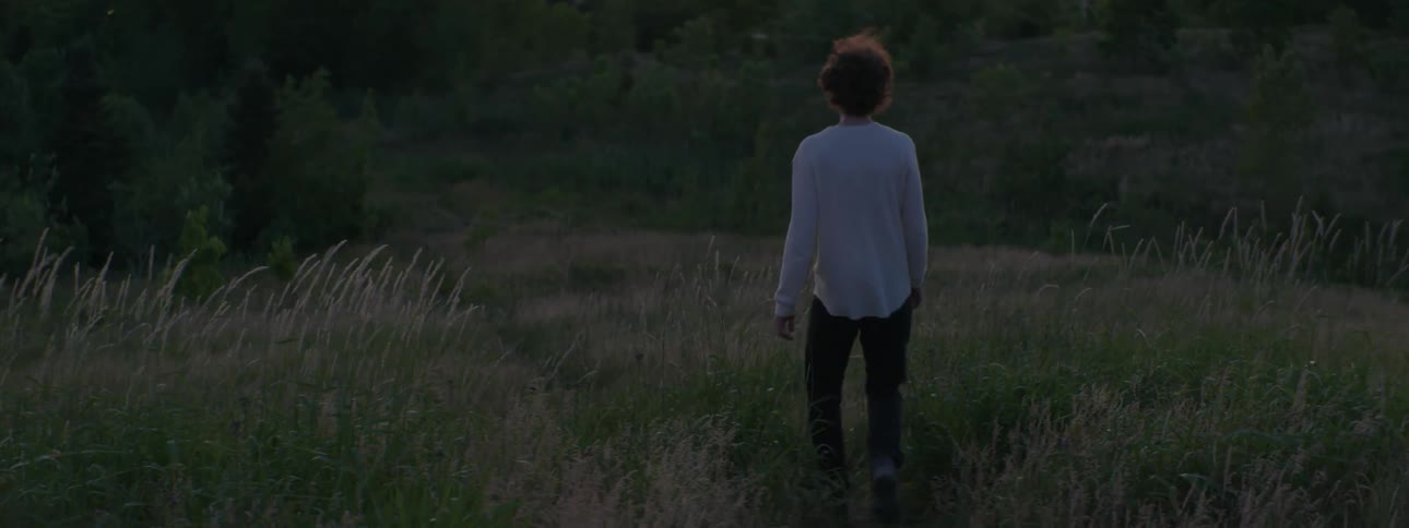 A man walks through a hilly countryside at sunset