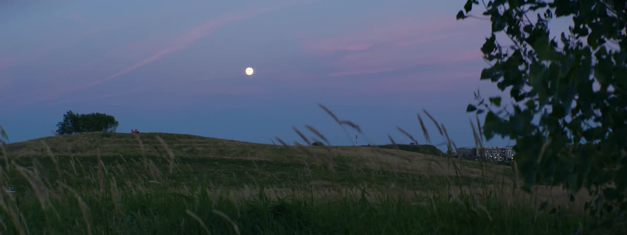 Moon sits in sky among red tinted clouds above hills and nearby town