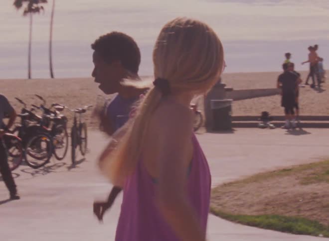 A crowd watches as a young man and woman dance on roller skates in a park