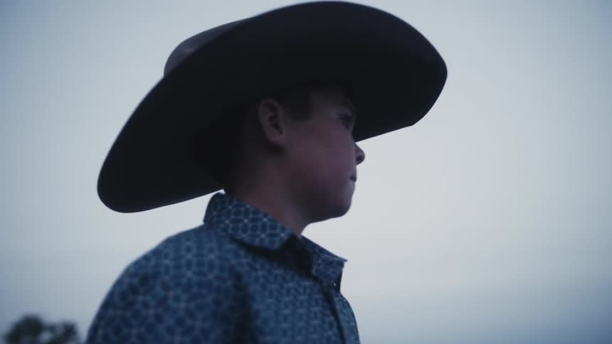 A young boy wearing a cowboy hats stands and stares into the distance