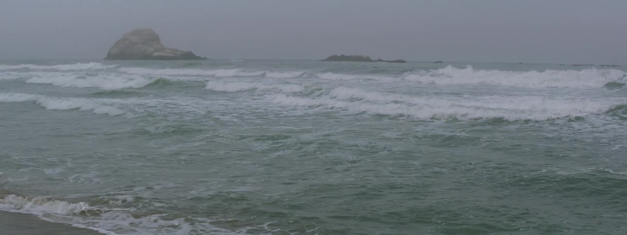 Ocean waves roll into a beach on a cloudy day