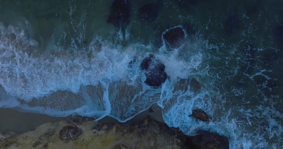 Ocean waves splash and foam against the rocks near the sandy shore