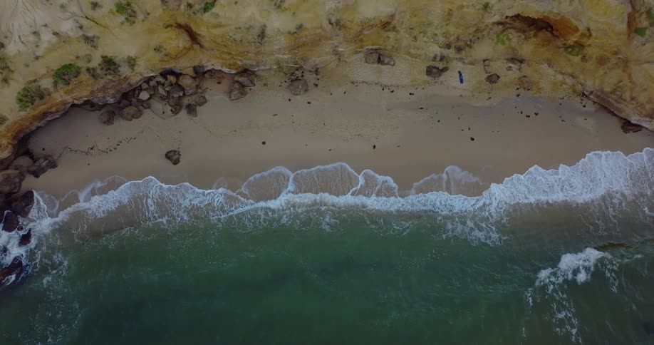 Waves crash onto a beach below a cliff