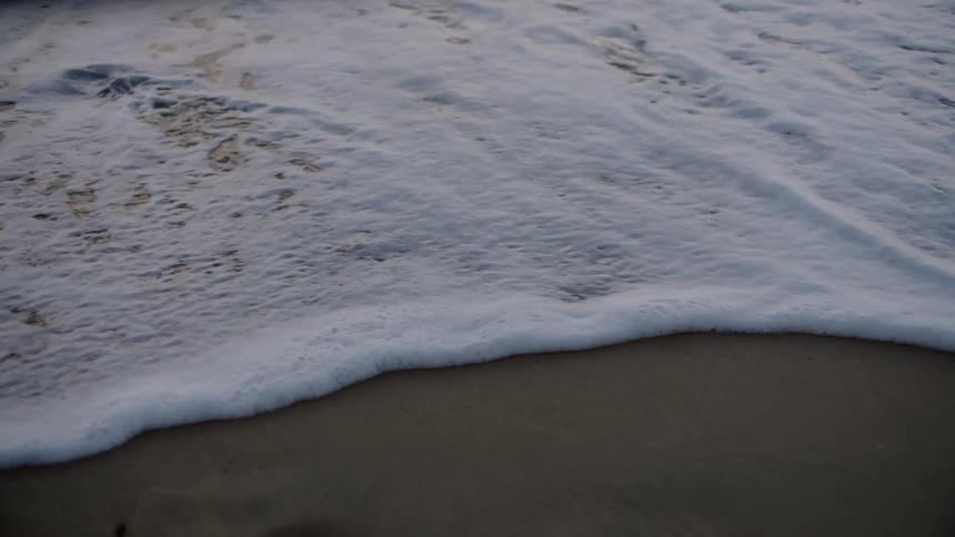 Waves crash onto beach spreading foam across the sand