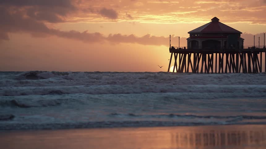 The sun is set low in the sky as ocean waves wash over a sandy beach