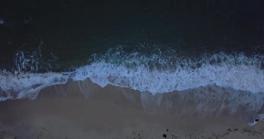 Multiple ocean waves wash upon a large sandy beach