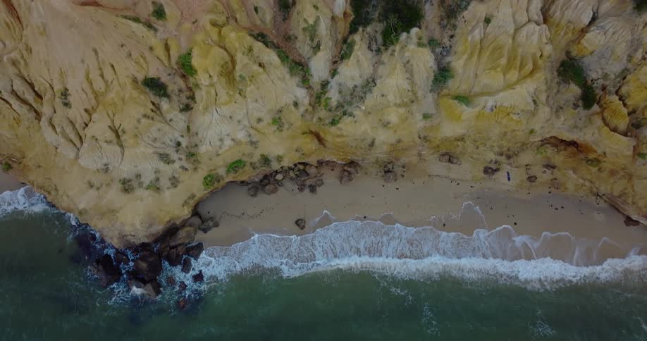 A tall cliff over a small beach next to the ocean during the day