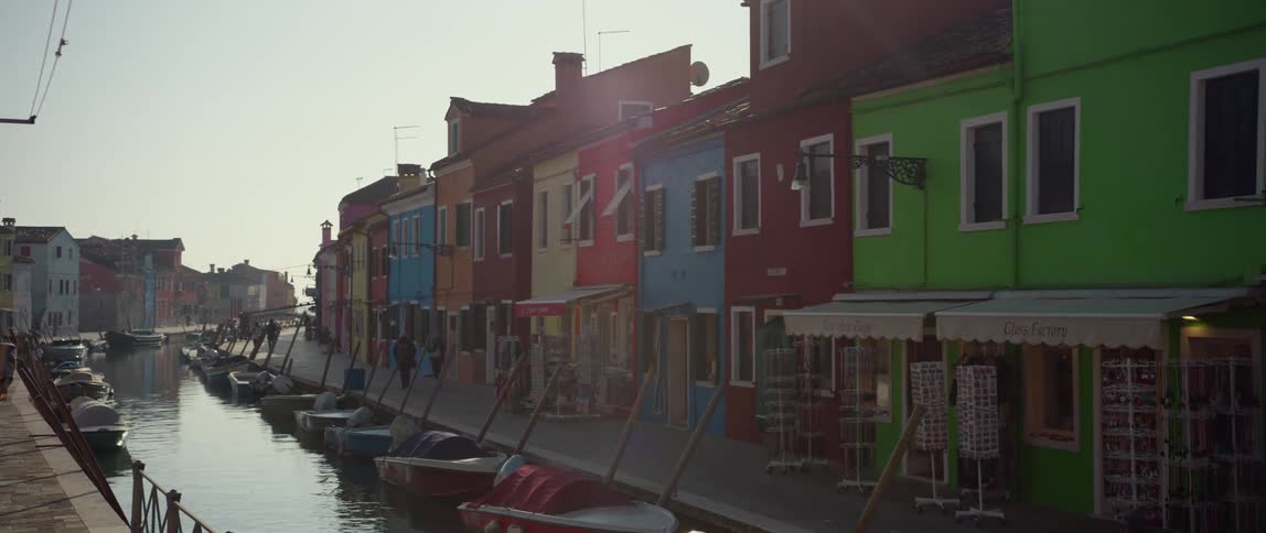 Boats docked in the canal in front of colorful bright homes and shops on Isola di Burano, Venice, Italy