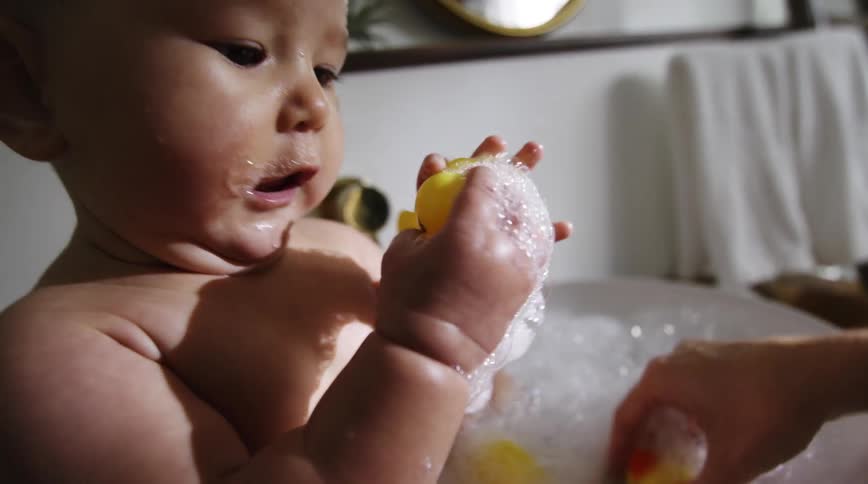 A baby plays with rubber ducks while sitting in a baby tub