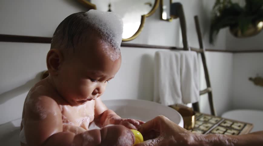 Mother washes baby who eating toy in bathroom sink
