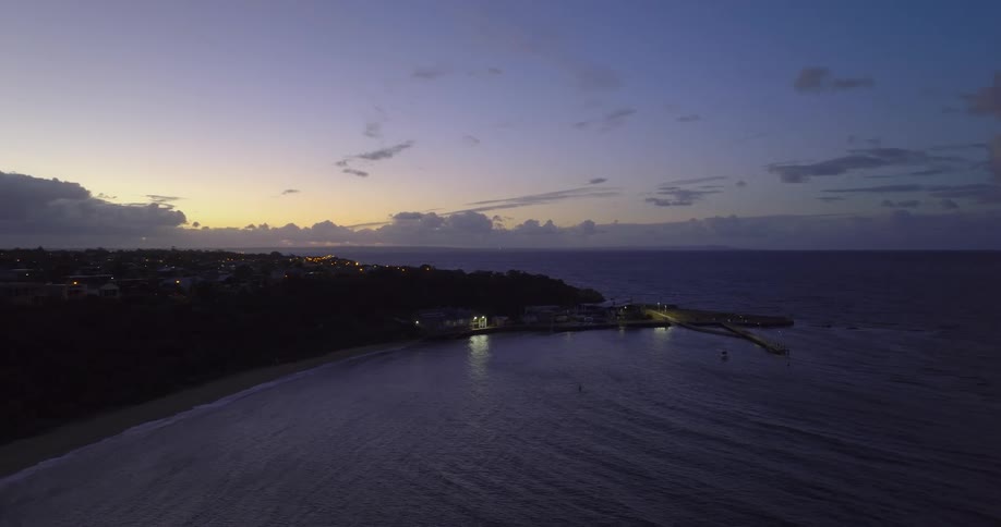 The sun has set below the horizon of a coastal area lined with several buildings