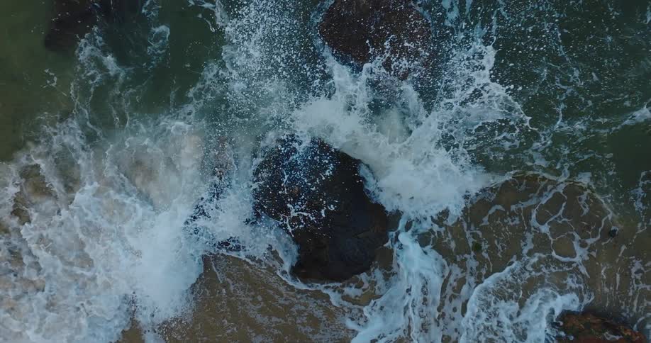 A birds eye view of waves crashing against a rock in the ocean