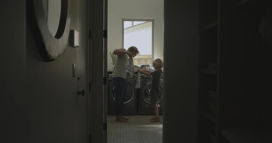 Dad standing in the laundry room with his son showing him how to fold laundry
