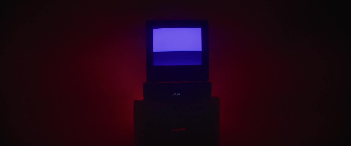 An older model cathode ray tube television flickers in a darkened room