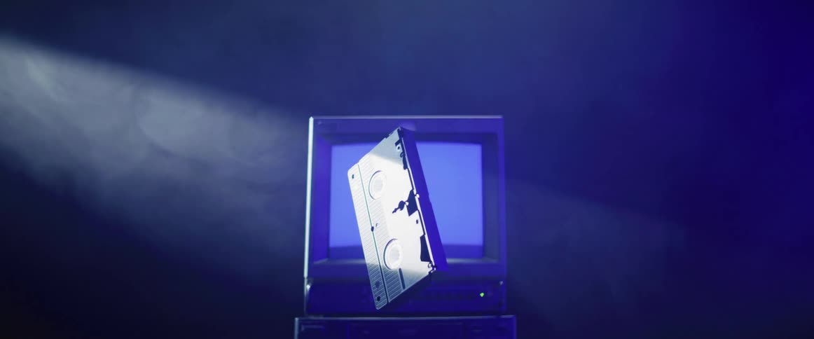 A video cassette spins in the air in front of a tube style television