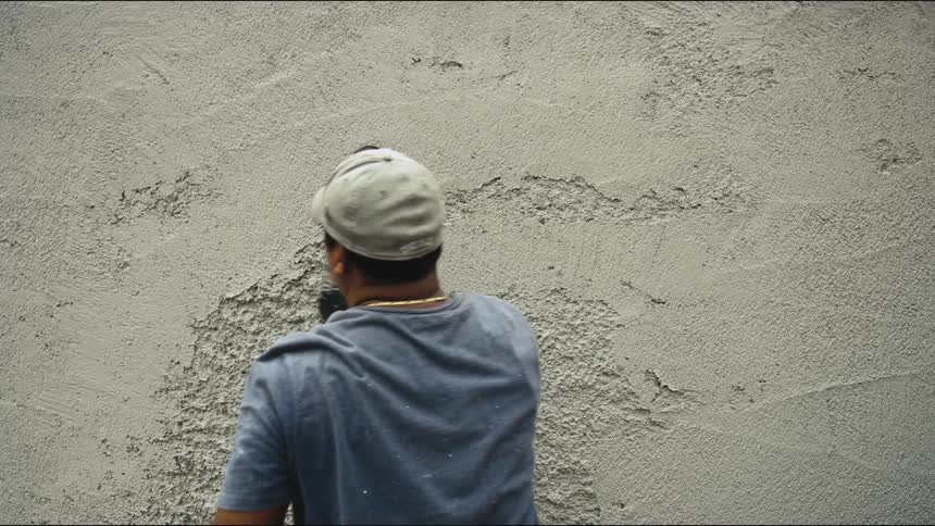 A man uses a flat tool to smooth out a wall made of concrete