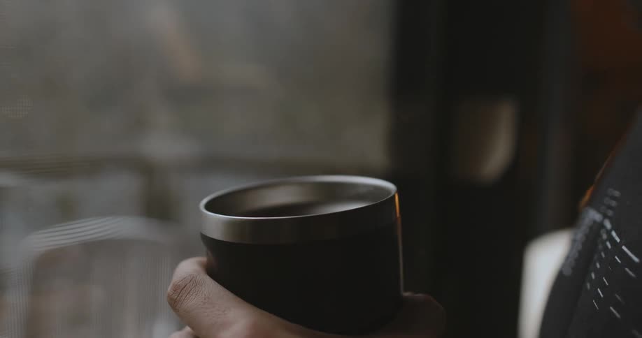 A man sips coffee from a travel mug while looking out his patio