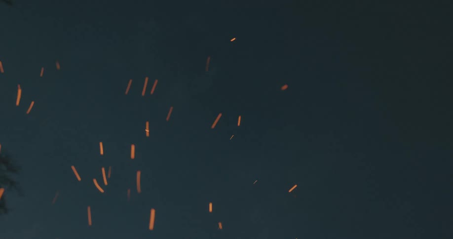 Embers from a fire float through the air outdoors at night