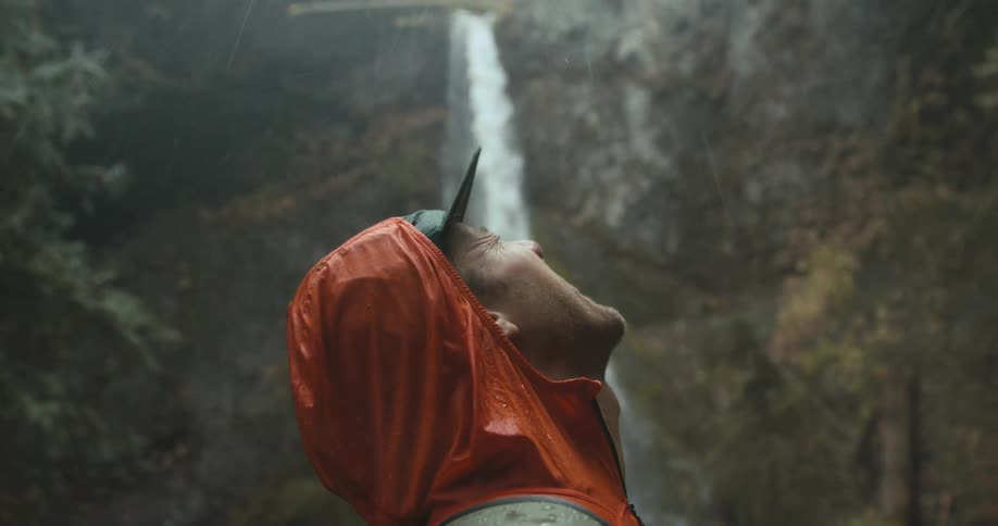 A man standing with his head back mouth open posing for a photograph that looks like he is swallowing the waterfall behind him