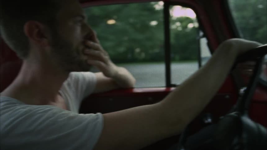 A young man drives a pickup truck through a rural town during the day