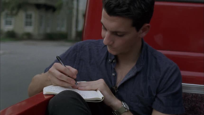 Man writing in a notebook while riding in the back of a red pickup