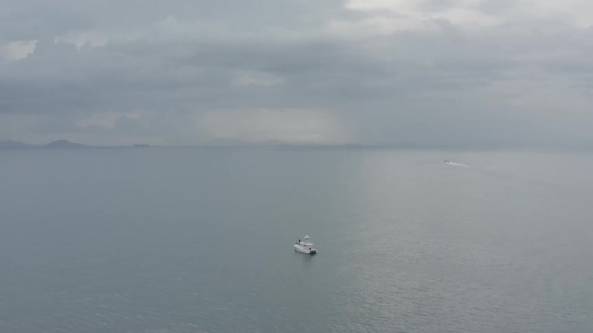 A boat sails in the water under a cloudy hazy sky