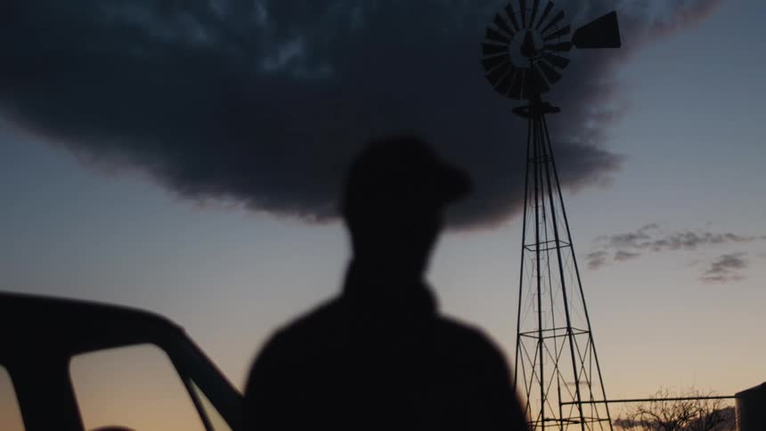 A man stands next to his vehicle and looks up at the dark clouds in the sky