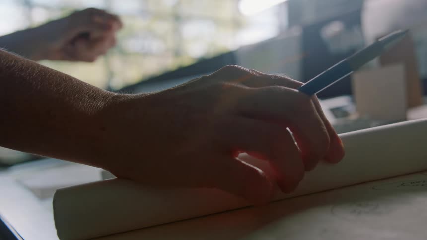 A person unrolls a sheet of paper on a desk and places a ruler on the surface