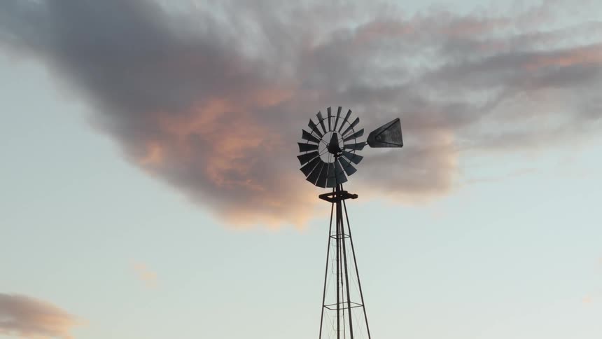 Farm windmill against an orange cloud at sunrise