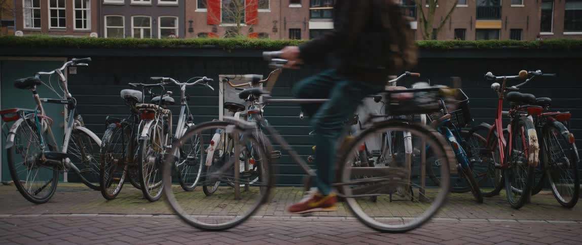Group of bicycles parked along a wall in Amsterdam as a cyclist peddles by
