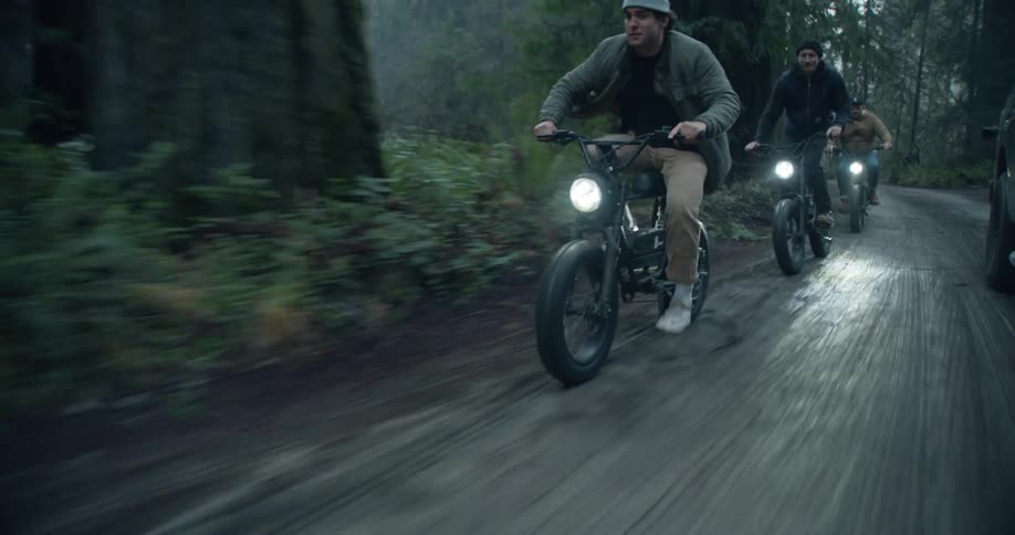 A group of men ride motorized bicycles along a road through a forest during the day