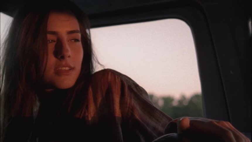A woman riding in a pickup truck looks at the road behind and smiles