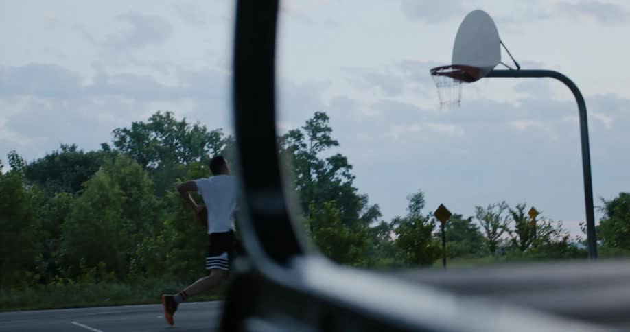 A man dribbles across an outdoor basketball court and dunks a basketball in the hoop