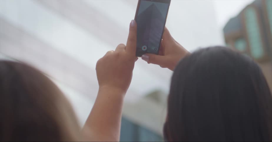 A woman uses a smartphone to photograph the facade of a building in a city during the day