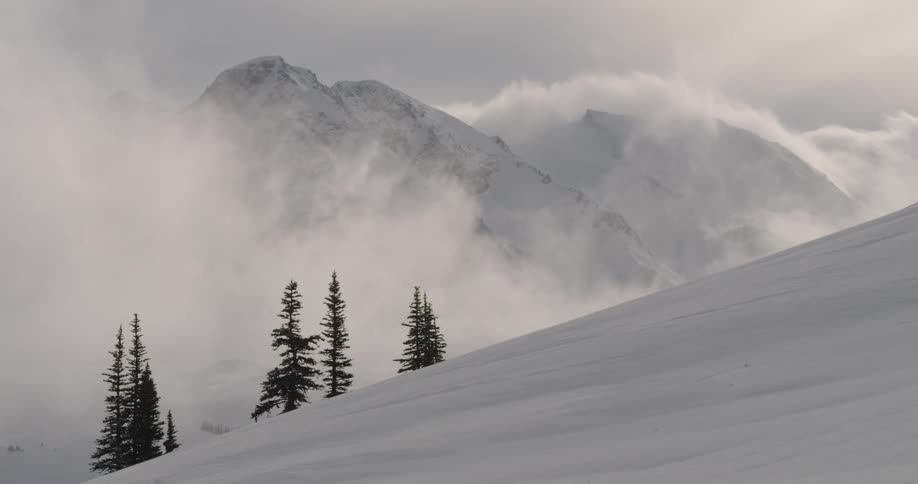 Fog blows across snow covered mountain slopes to reveal jagged peak
