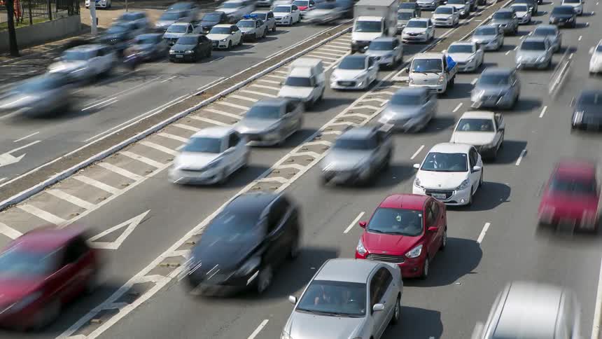 Dense traffic travels along a wide motorway in a city during the day
