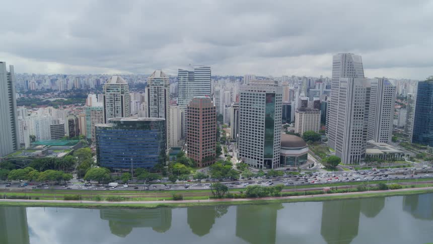 Vehicles travel on the highway between the city buildings and a river on a cloudy day