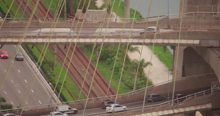 A vehicle travels across a multilevel bridge over a river during the day