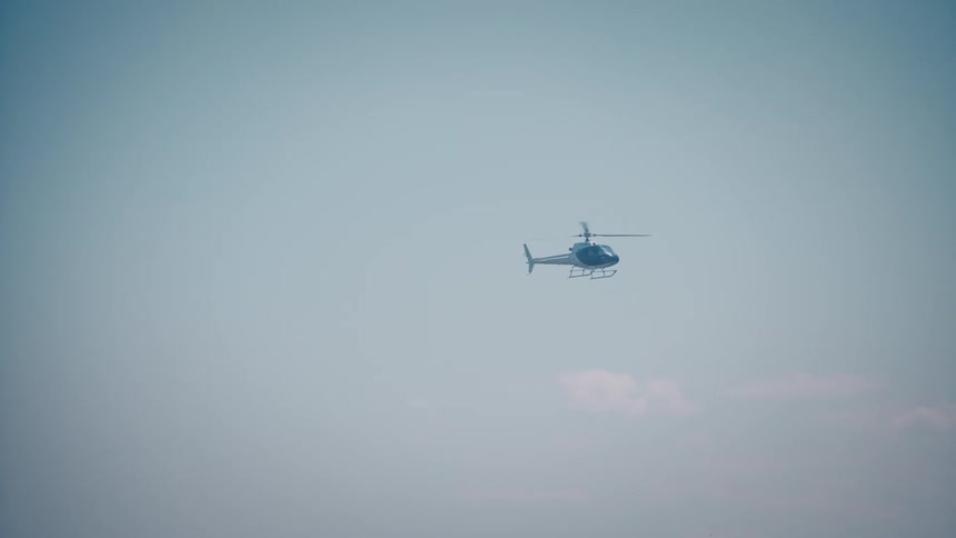A helicopter hovers in the sky with a metropolitan skyline visible in the distance