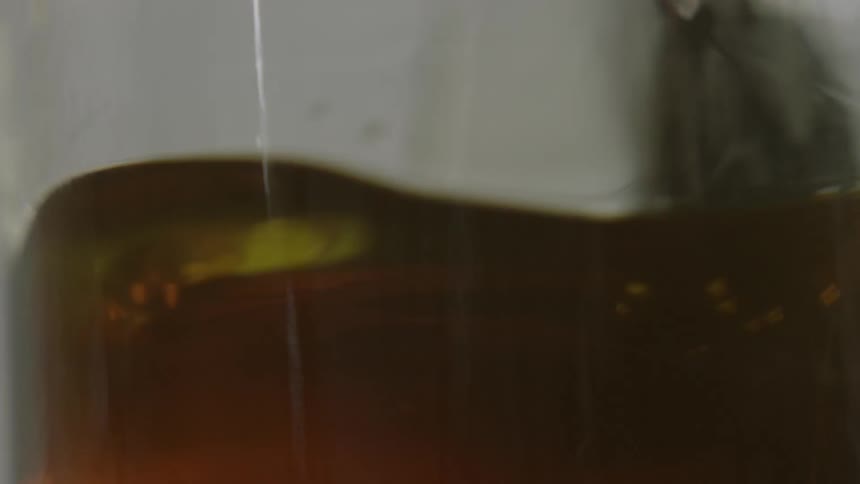 A person dips a brush into brown liquid