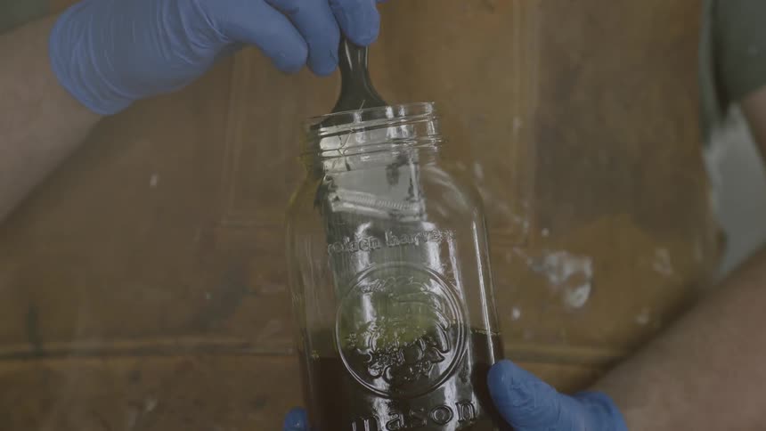 A paint brush narrowly fits into a jar of stain