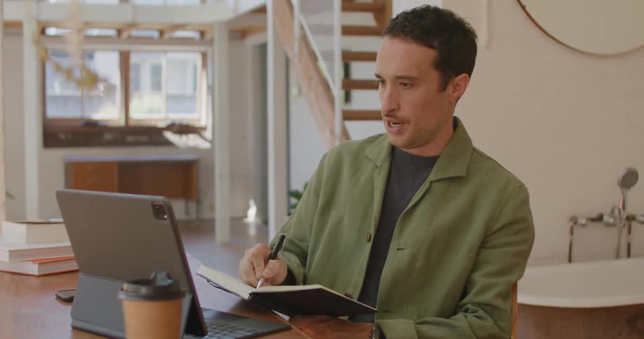 A man talking on a video call while writing in a notebook