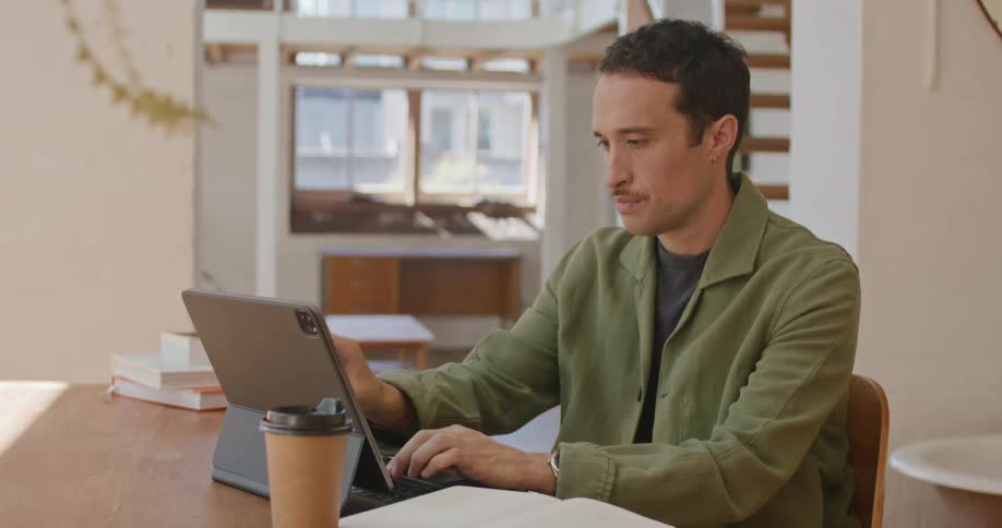 A man typing on a tablet and fidgeting with a pen while working at a desk