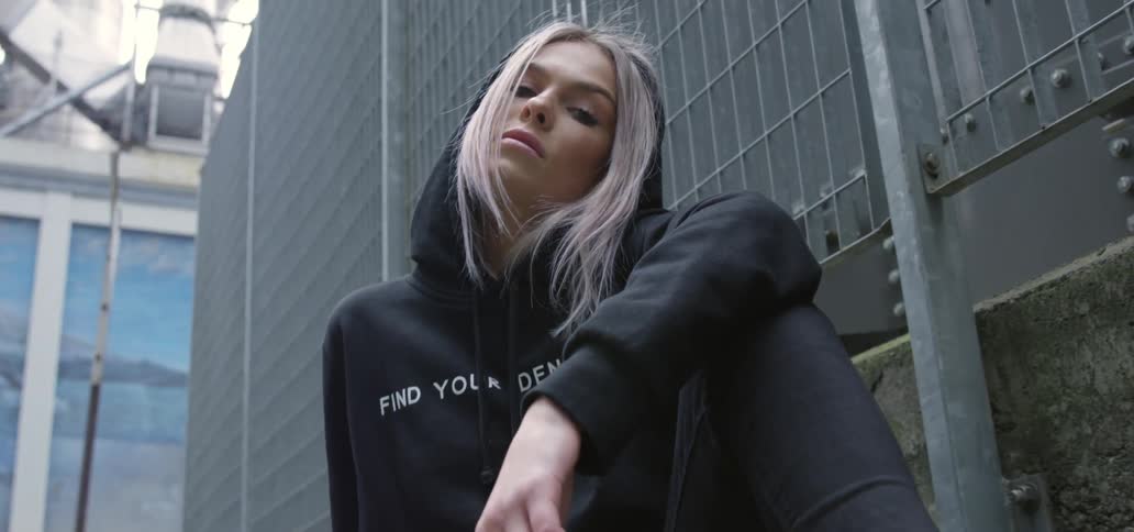 Blonde woman wearing a black hoodie sitting on the ground at the sidewalk