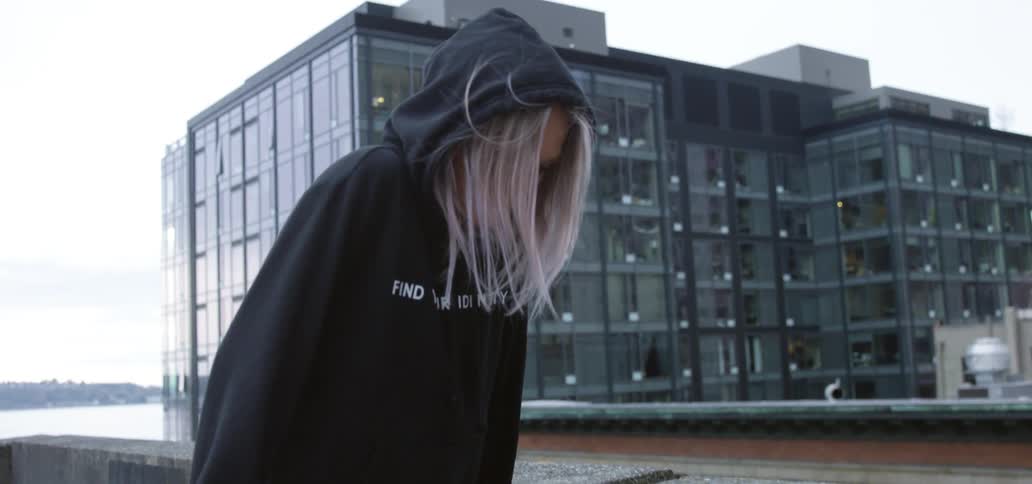 A sad teenager stands on a rooftop with her head down