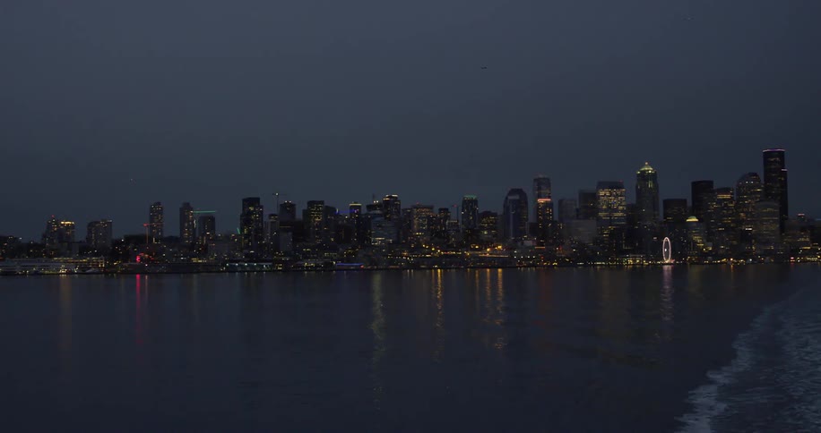 Vessel leaves wake as it move away from brightly lit city at night