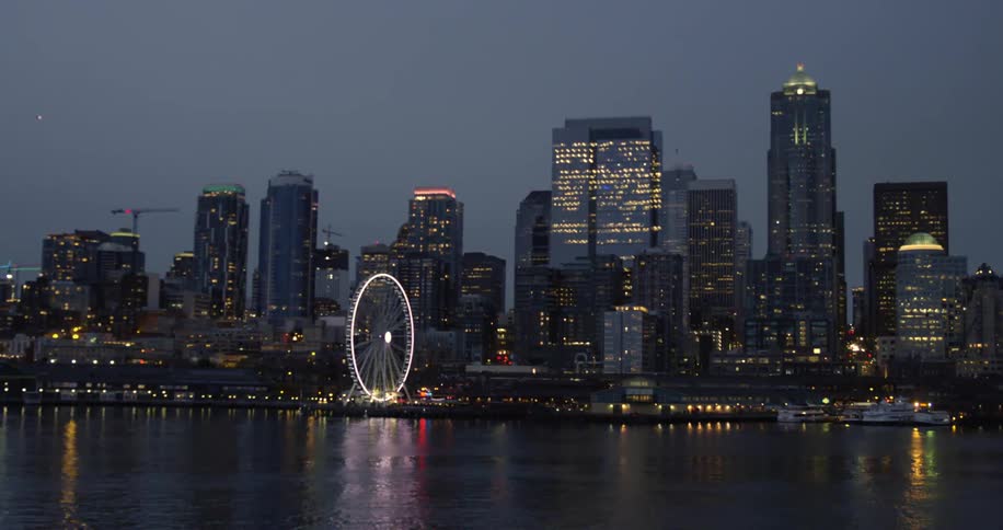 Illuminated high rise buildings and ferris wheel seen from traveling boat at night