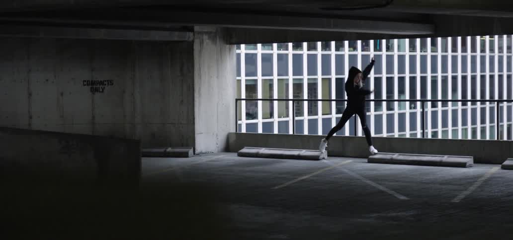 A woman in a hoodie balancing on concrete in a parking garage