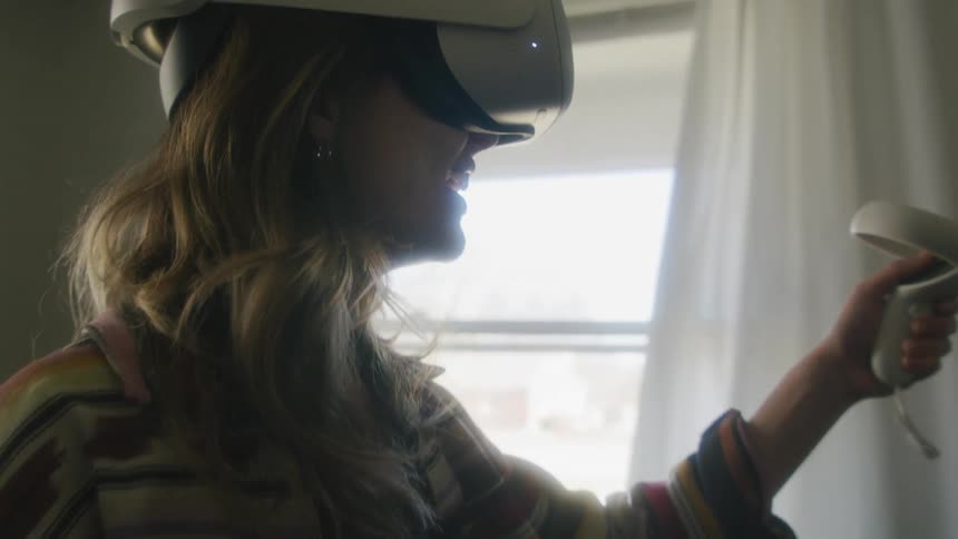 Woman with brown wavy hair equipped with a vr headset and motion controllers uses virtual reality in living room at home